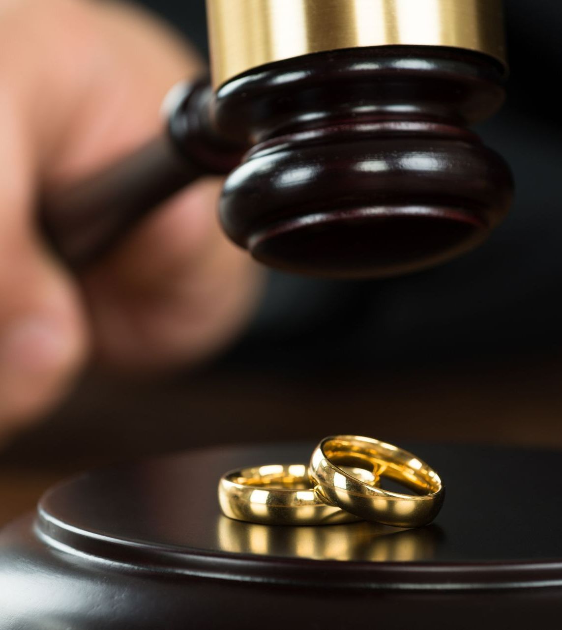 A gavel poised above two golden wedding rings, likely symbolizing a divorce proceeding.