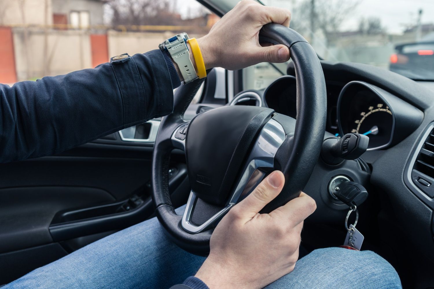 A man is driving a car with his hands on the steering wheel.