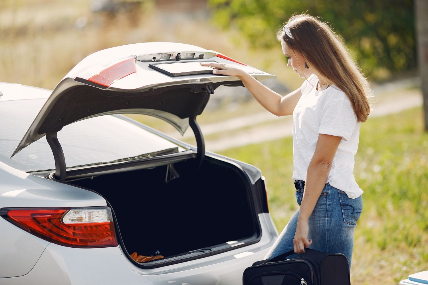 A woman is loading her luggage into the trunk of a car.