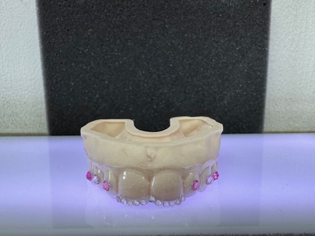A model of teeth with pink gems, beige color, sitting on a purple surface with a black background.