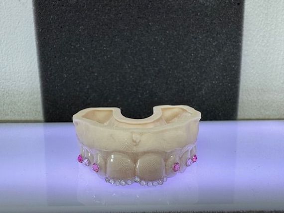 A model of teeth with pink gems, beige color, sitting on a purple surface with a black background.