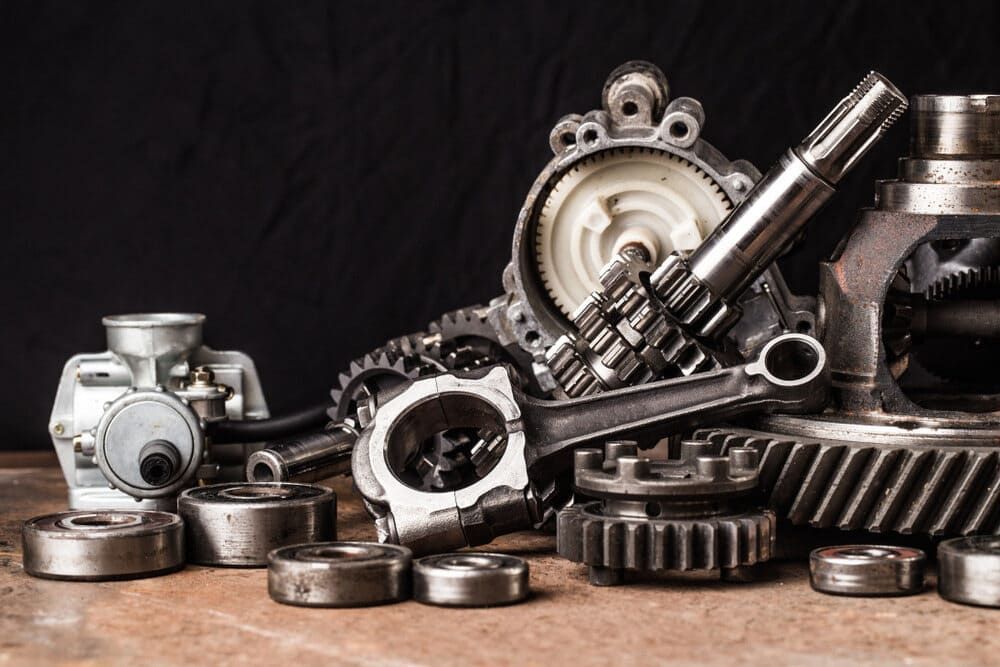 Collection of mechanical parts and gears, including bearings, shafts and cogs, arranged on a bench