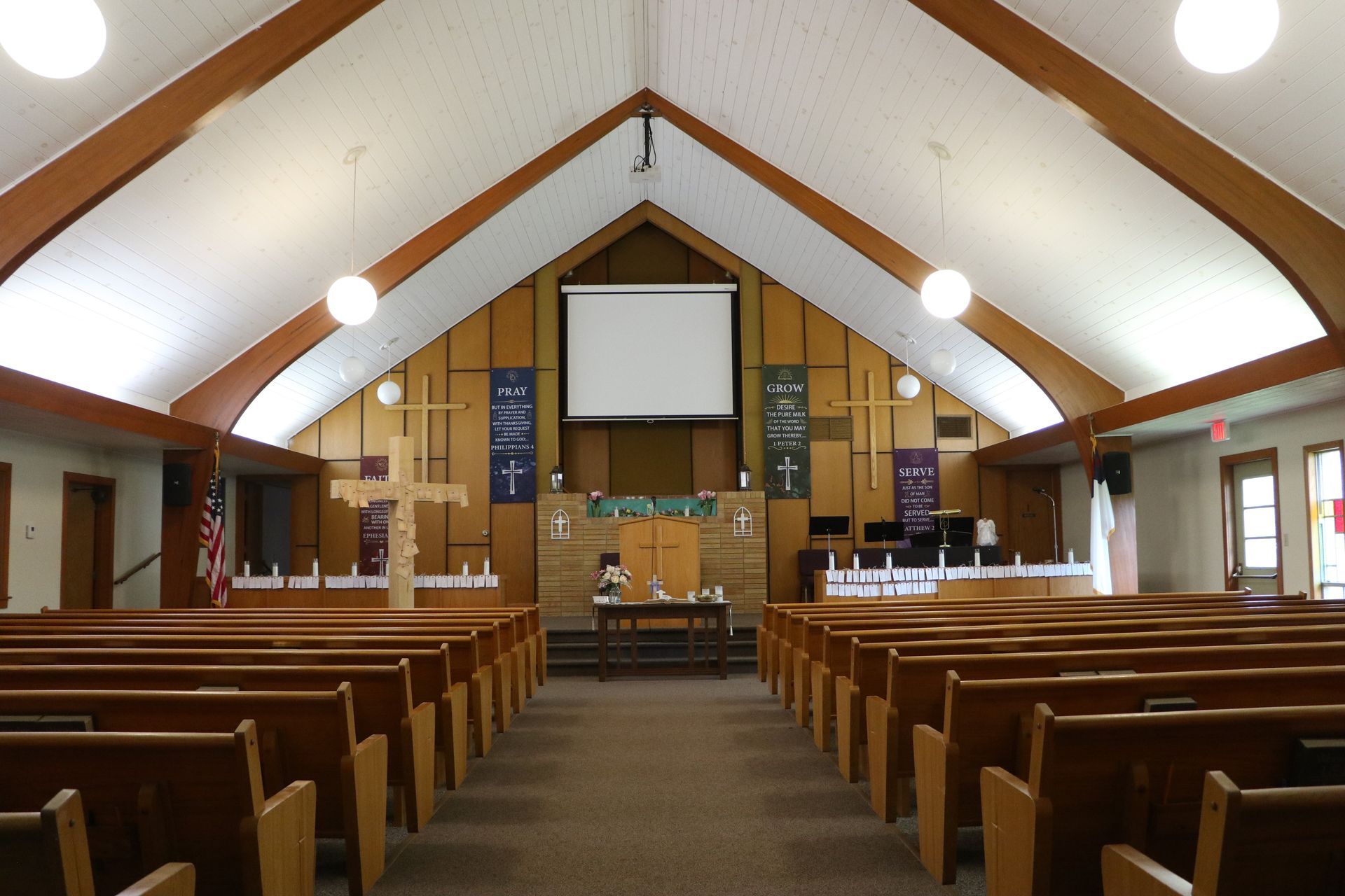 An empty church with rows of wooden benches and a projector screen