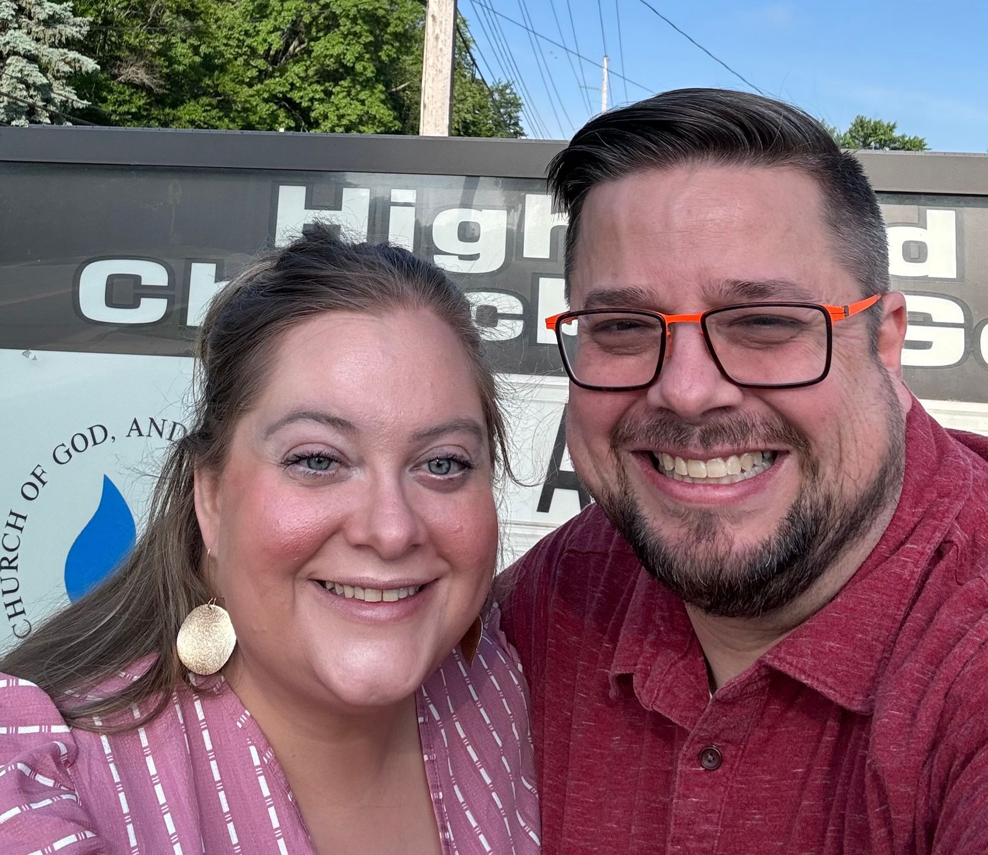 A man and a woman are posing for a picture in front of a church sign.