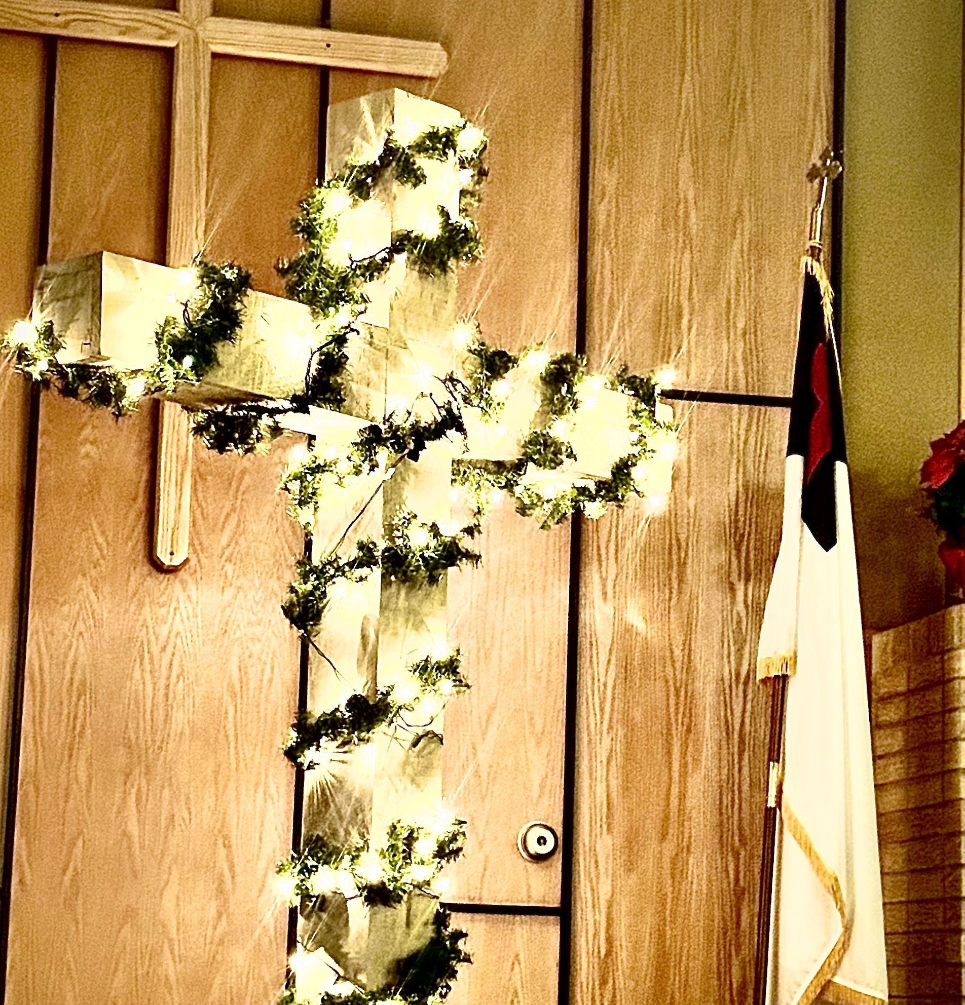 A wooden cross is decorated with flowers and lights