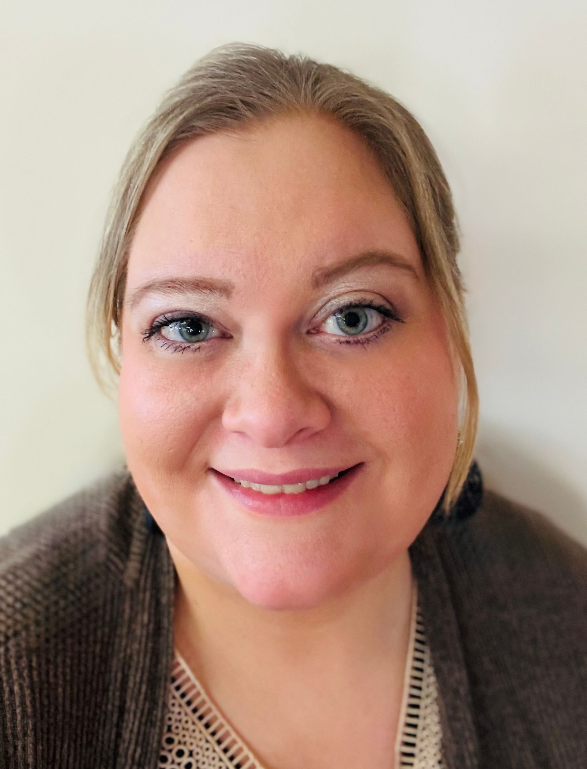 A woman is smiling for the camera and wearing a brown sweater.