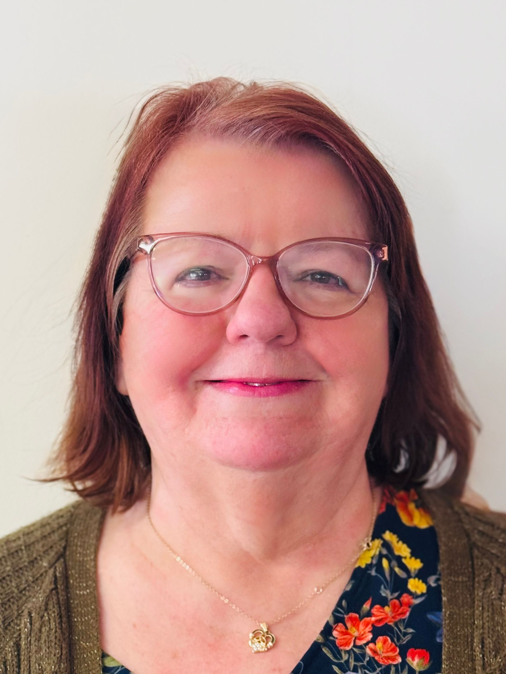 A woman wearing glasses and a necklace is smiling for the camera.