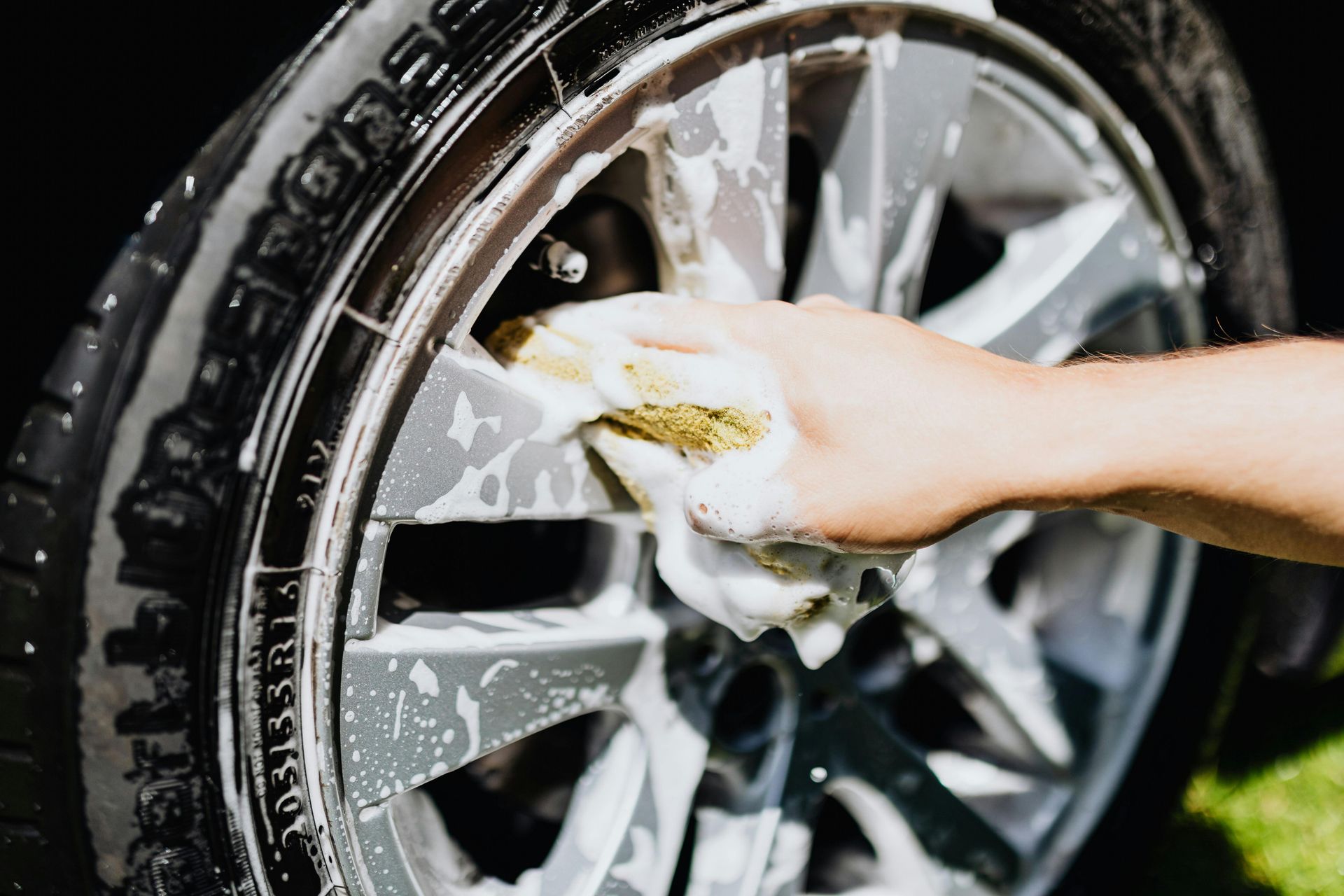 A person is washing a car wheel with a sponge.