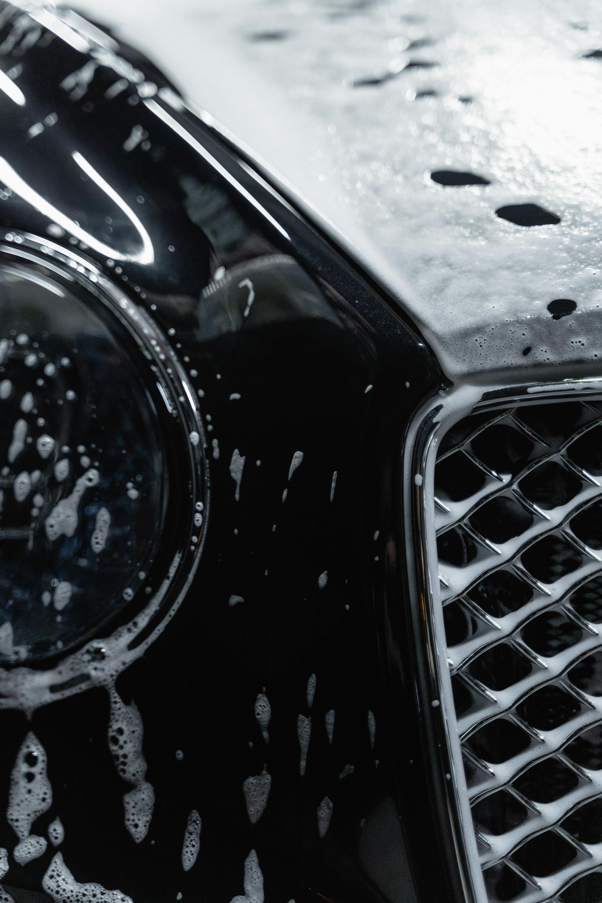 A close up of a black car 's headlight and grill covered in soap.