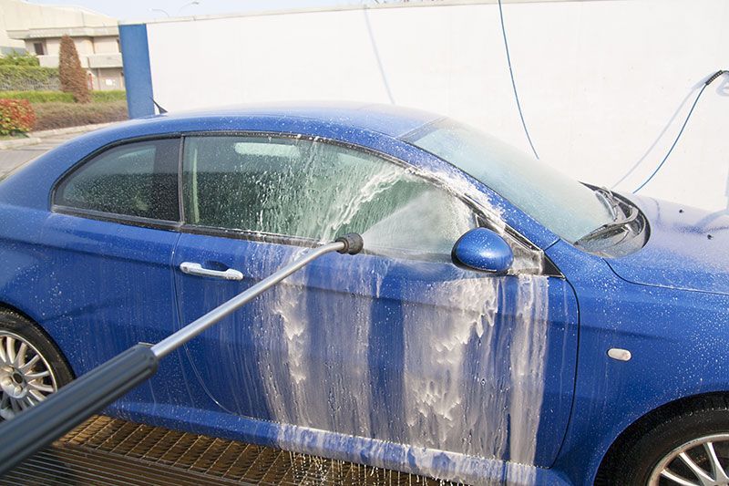 A blue car is being washed with a high pressure washer