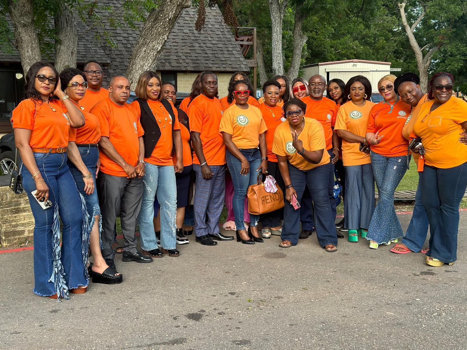 A group of members of Akisan Katy wearing orange shirts and blue jeans are posing for a picture.