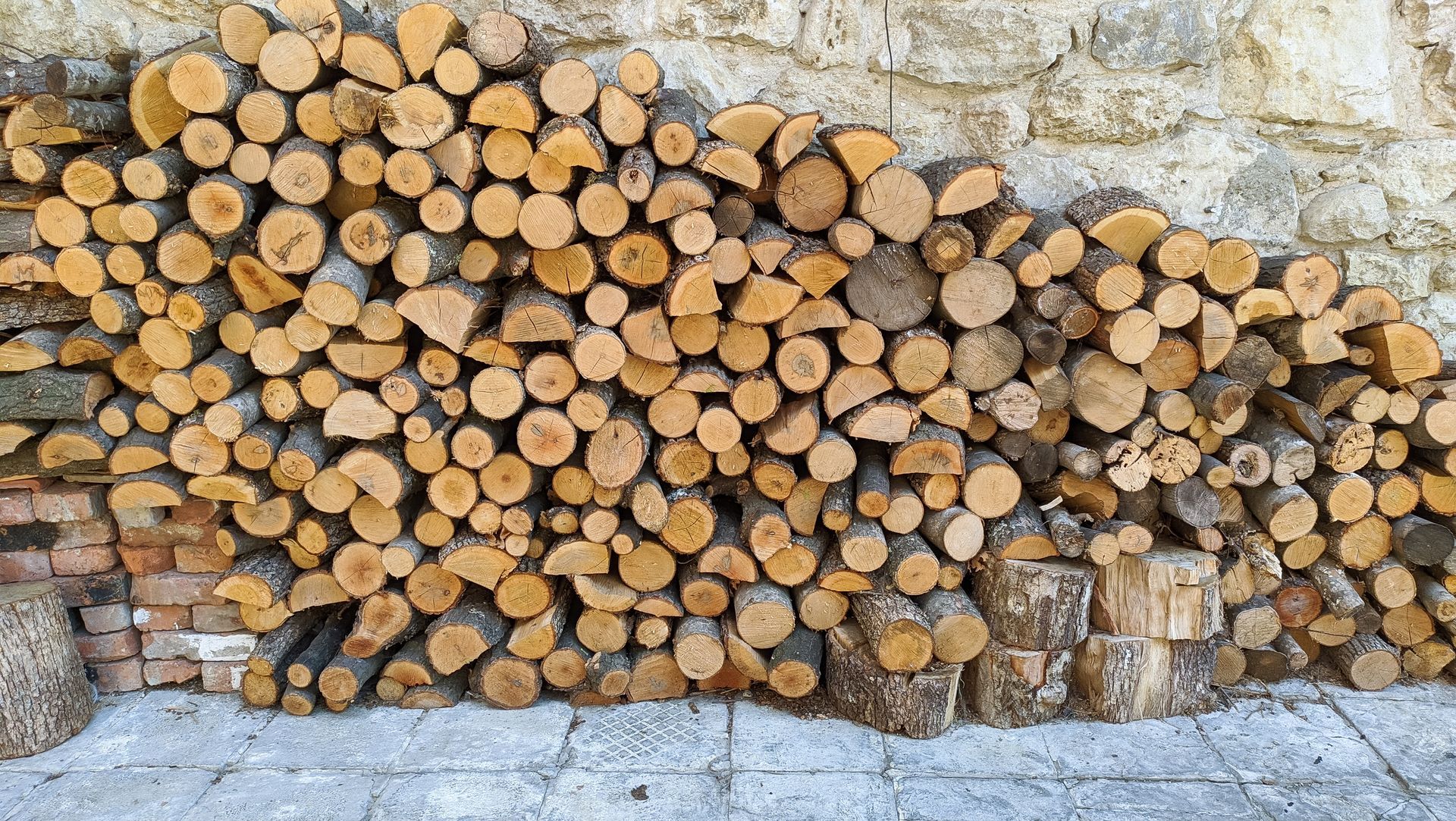 Pile of Stacked Firewood Against a Stone Wall and Brick Base — Tenterfield Timber & Hardware in Tenterfield, NSW