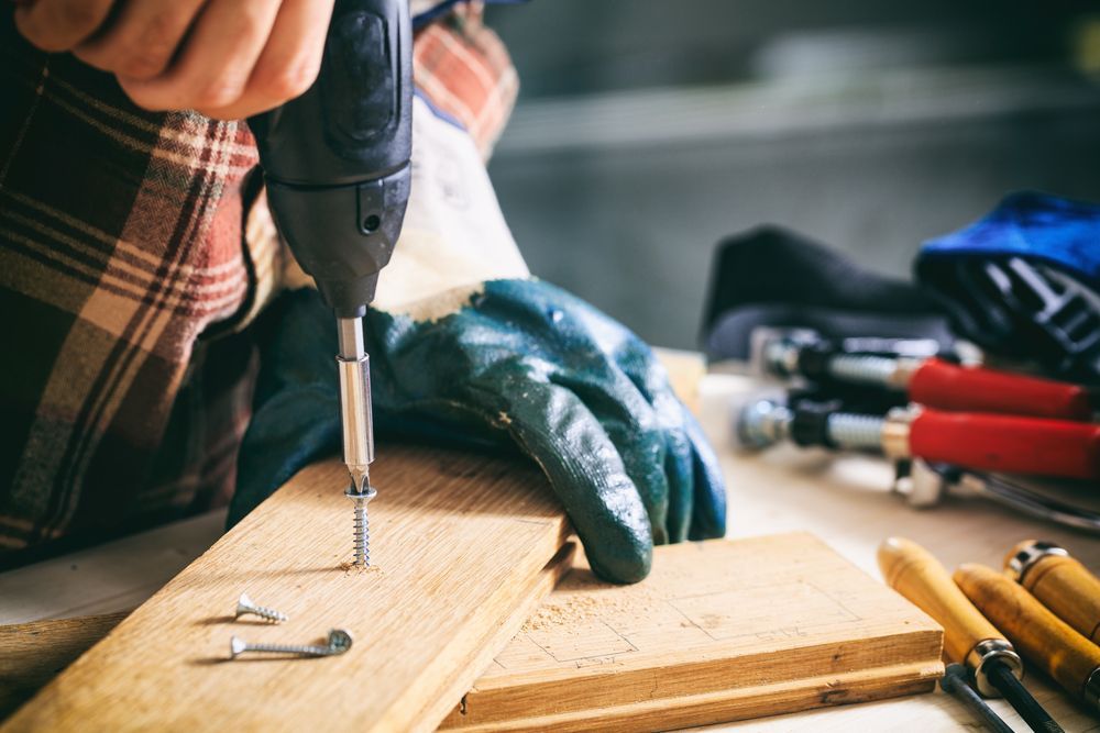 Person Using a Power Drill to Screw a Screw Into a Wooden Plank — Tenterfield Timber & Hardware in Bonshaw, NSW