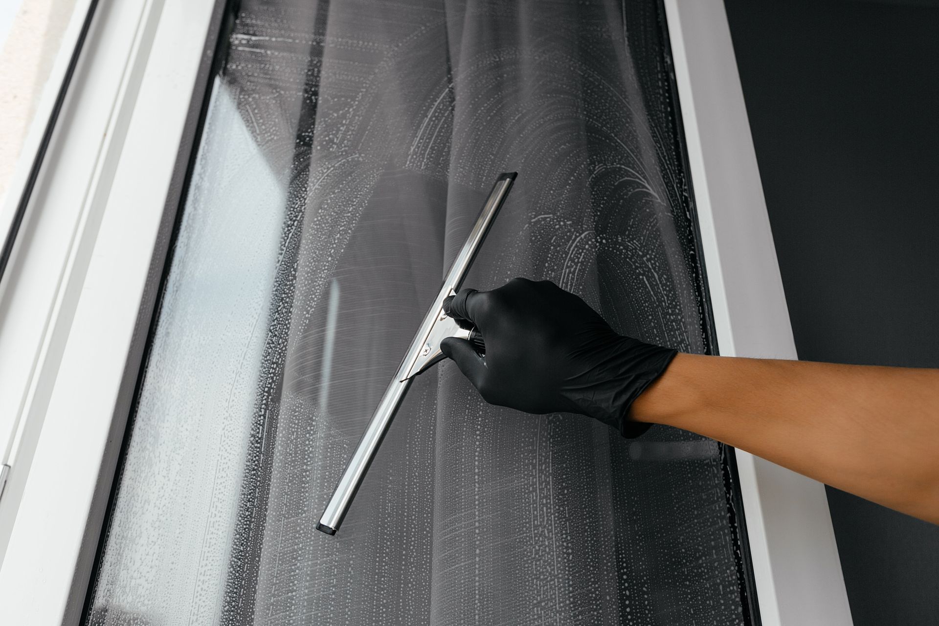 Person in black glove using a squeegee to clean a window.