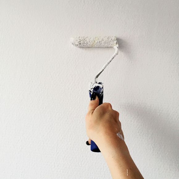 A person is painting a wall with a paint roller.