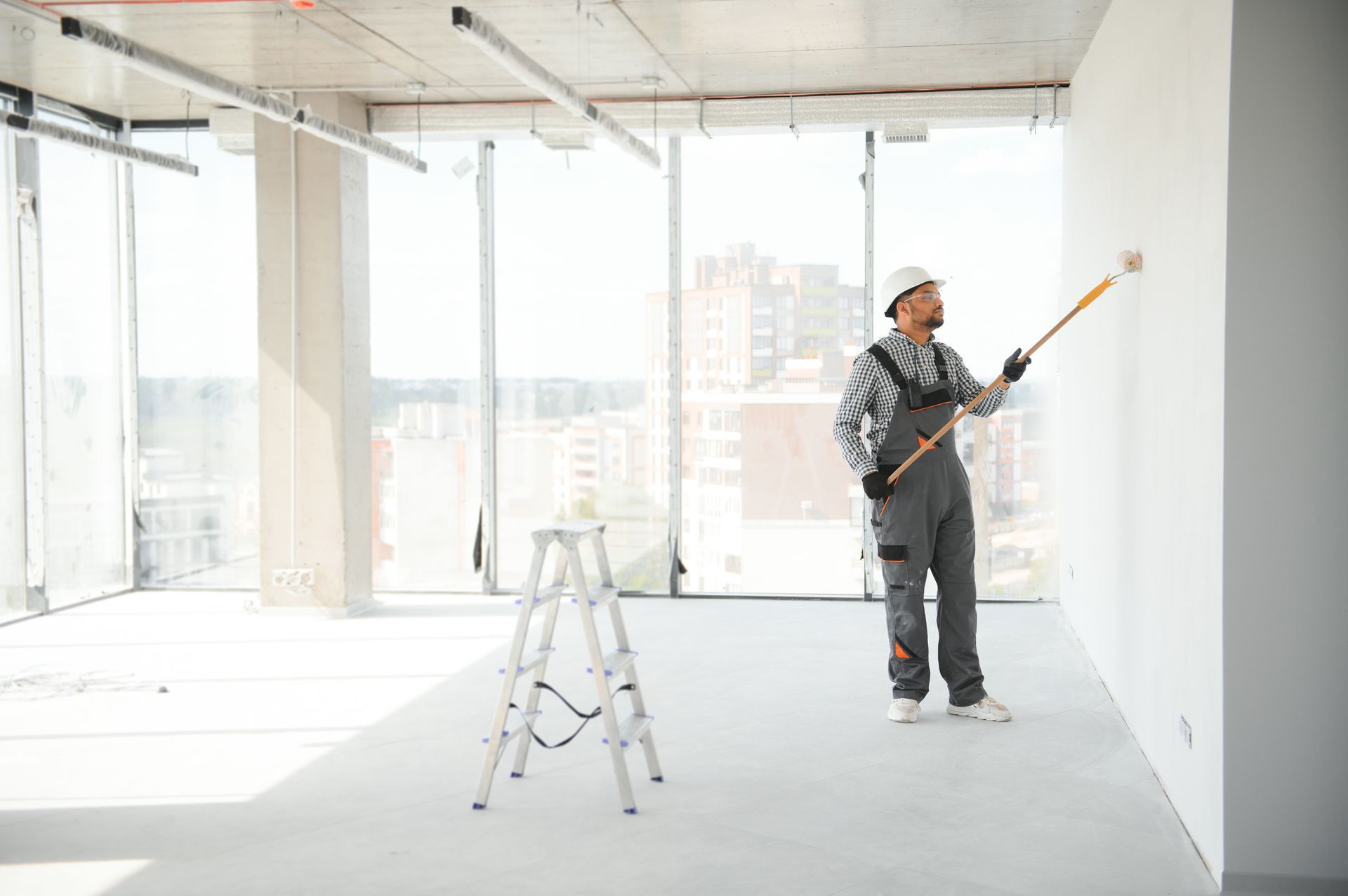 A man is painting a wall with a roller in an empty room.
