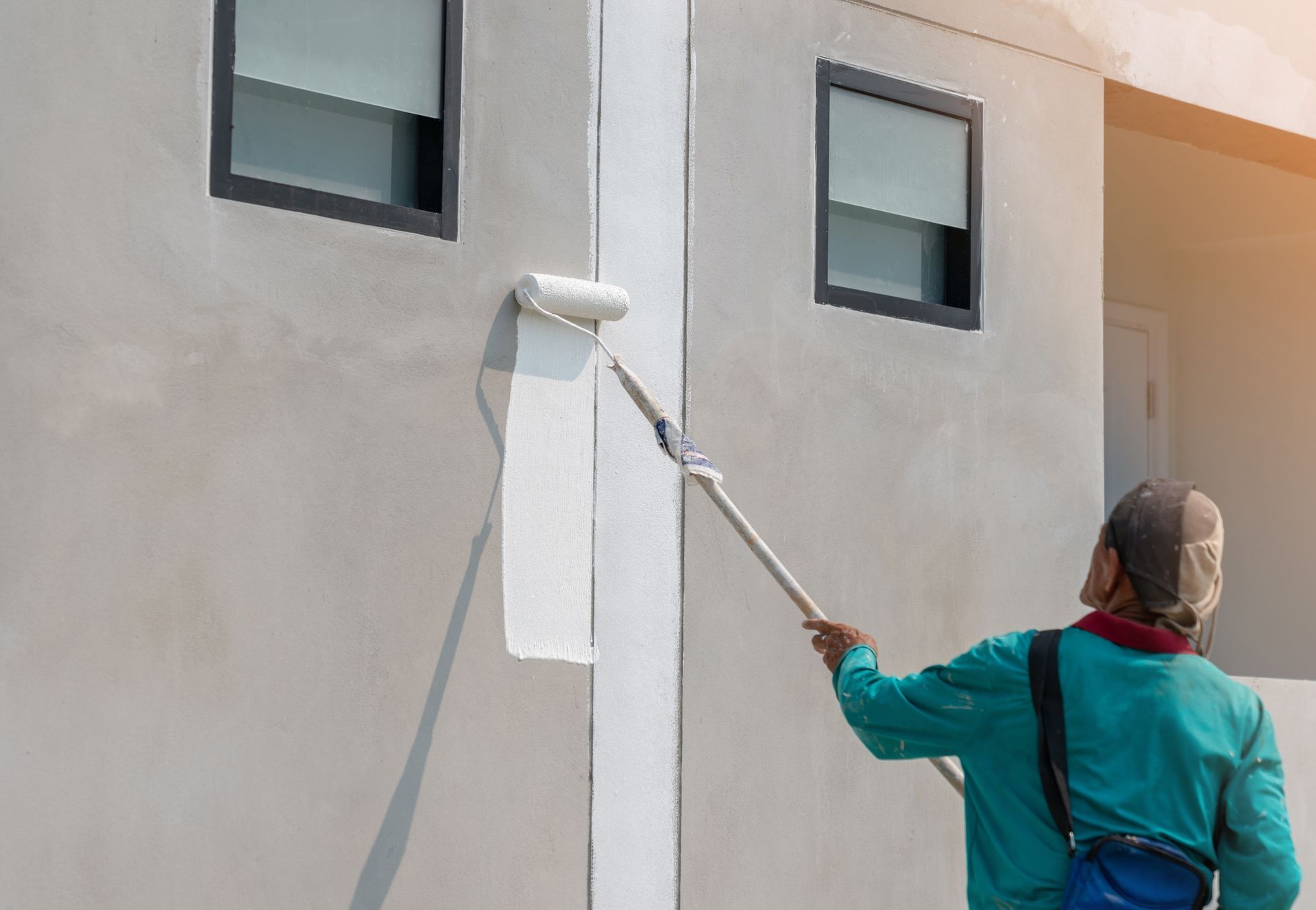 A man is painting the side of a building with a paint roller.