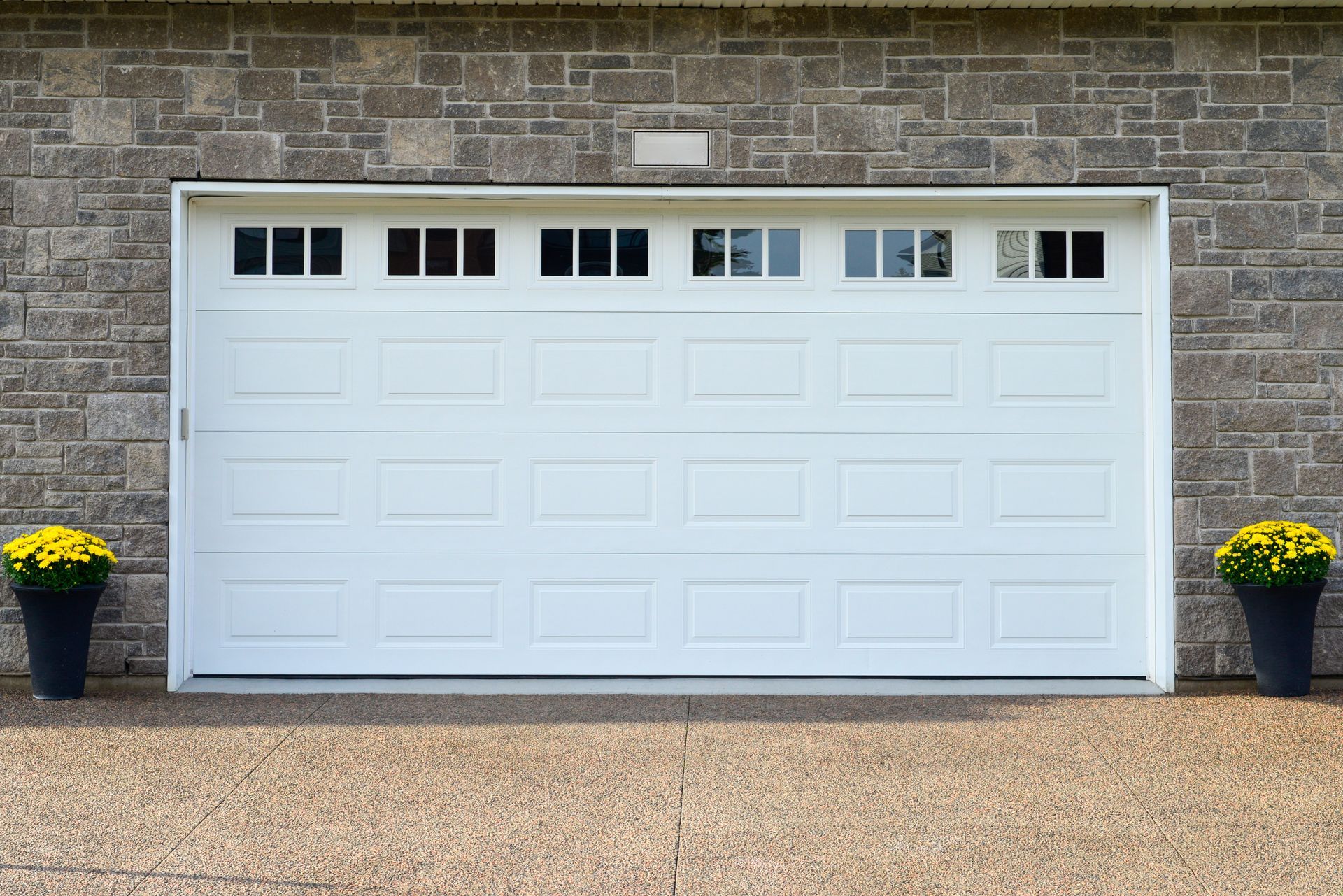 White garage door with window panels, set against a brick wall. Yellow potted flowers flank either side of the entrance.