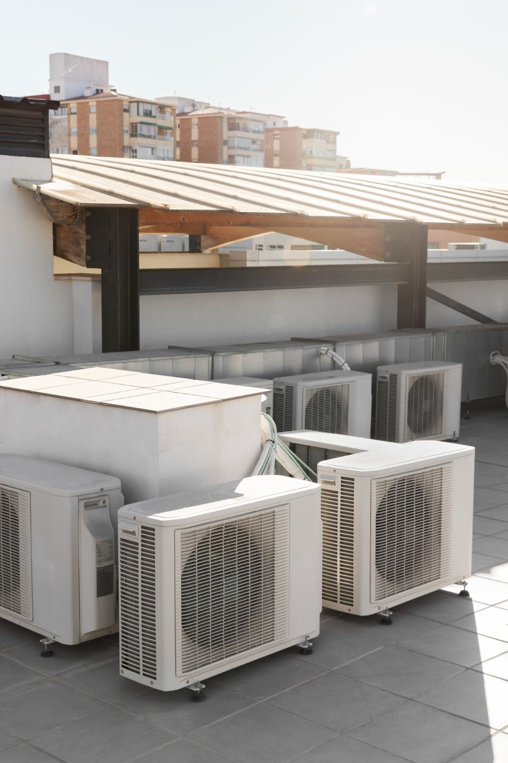 Air conditioning units on a rooftop under a wooden overhang, sunny day.