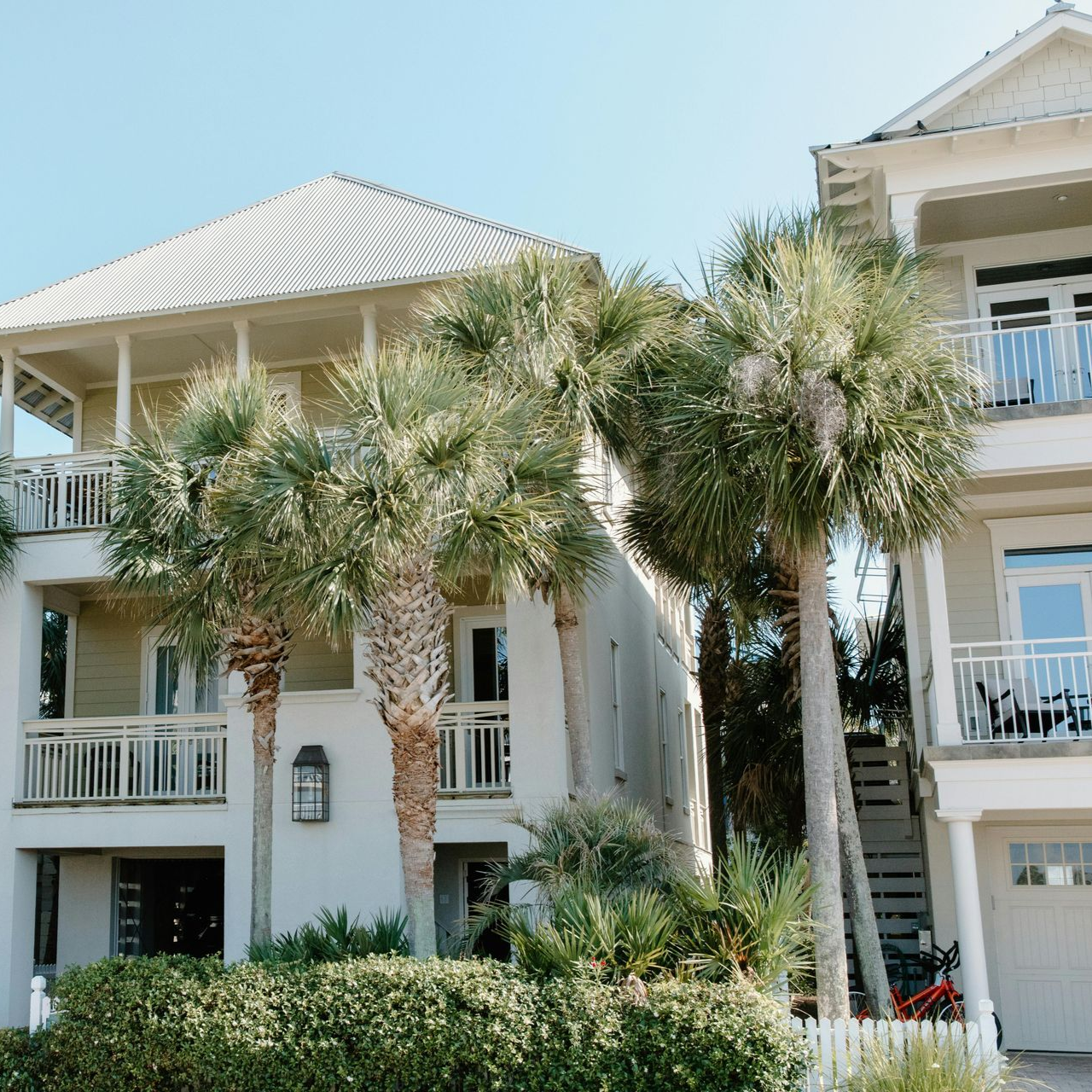Two-story beach houses, white siding, balconies, palm trees, blue sky.
