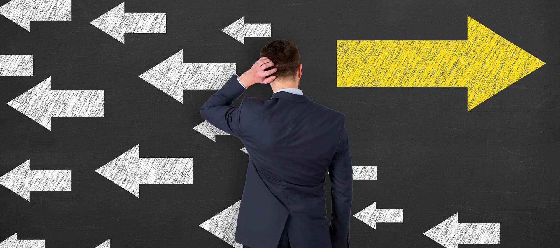 man looks at chalkboard with many small arrows pointing left and one large arrow pointing right