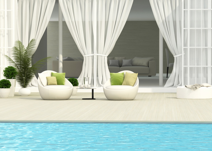 View looking over a pool to modern egg chairs with cushions, framed by tied back opaque curtains forming outdoor room.