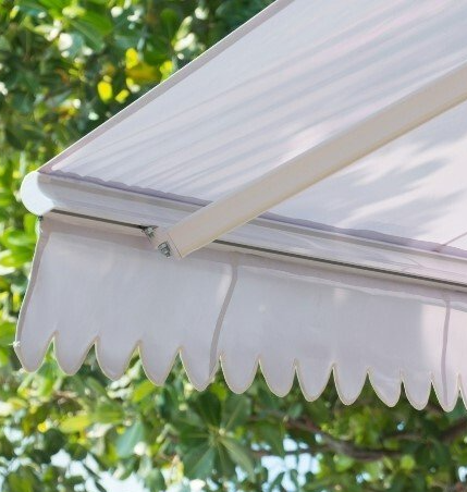 Close up of corner of extended white outdoor awning, with green trees in background.