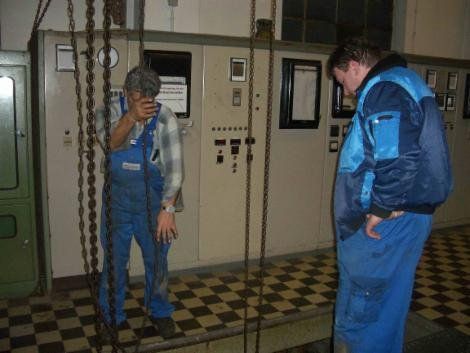 Zwei Arbeiter in blauen Overalls in der Nähe eines Bedienfelds in einer Industrieanlage.