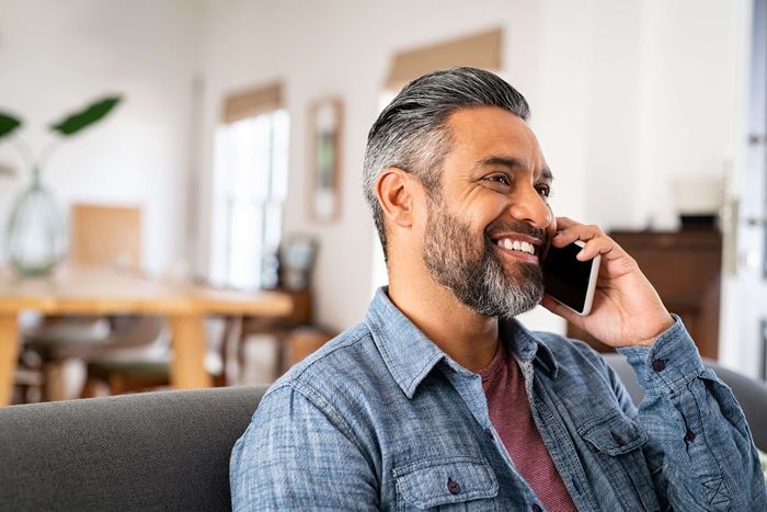 A man is sitting on a couch talking on a cell phone.