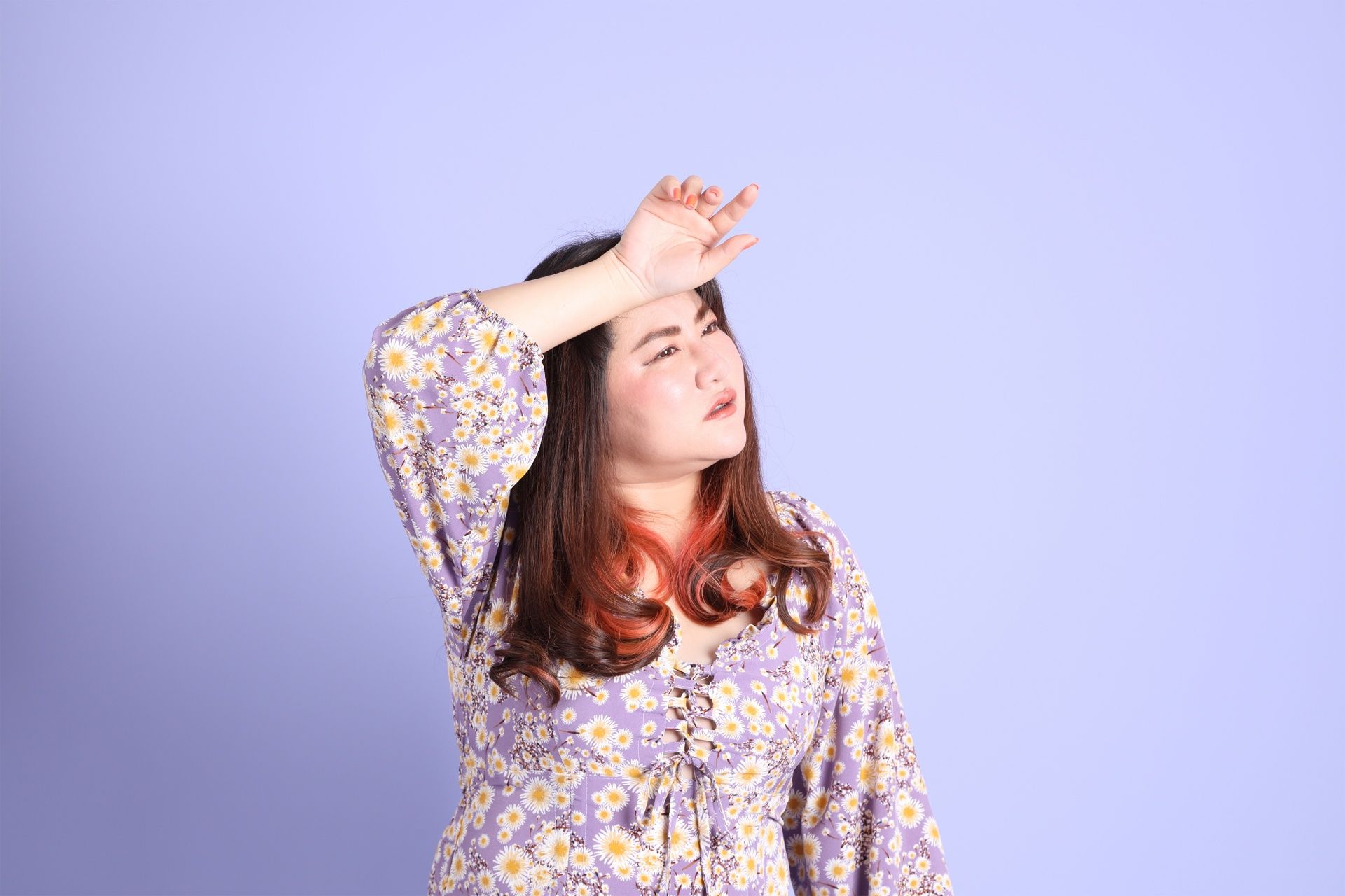 A woman in a purple dress is covering her face with her hand.