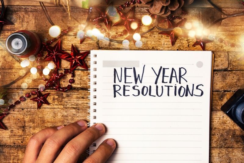 A person is holding a notebook with the words `` new year resolutions '' written on it.