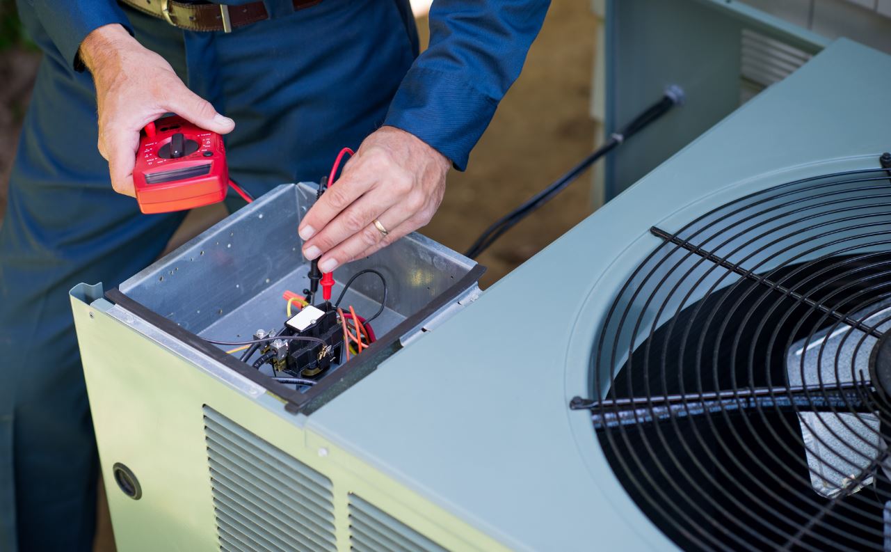 A man is working on an air conditioner with a multimeter.