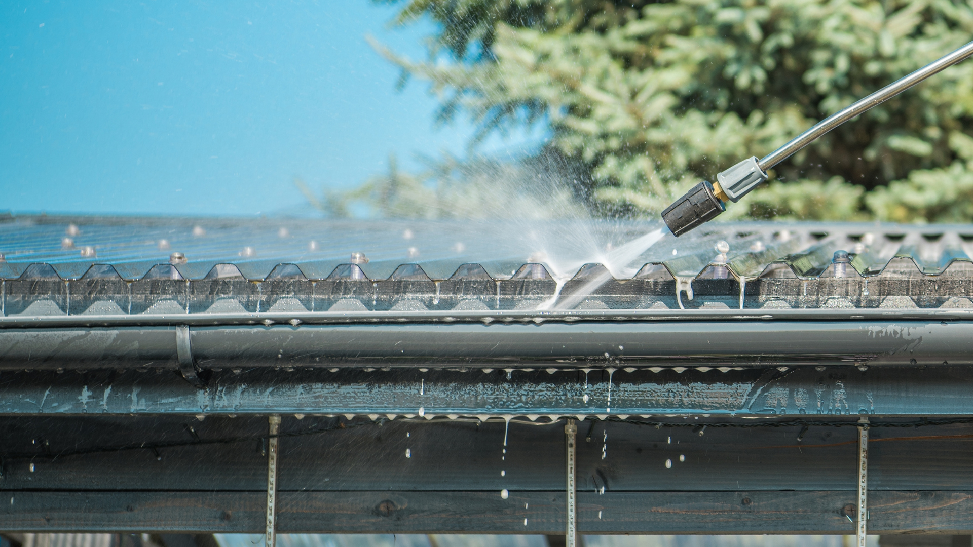 A person is cleaning a gutter with a high pressure washer.