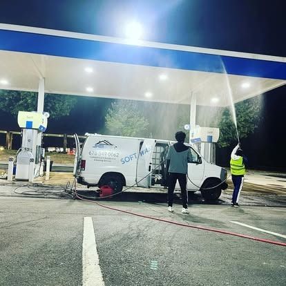 A man is washing a van at a gas station at night.