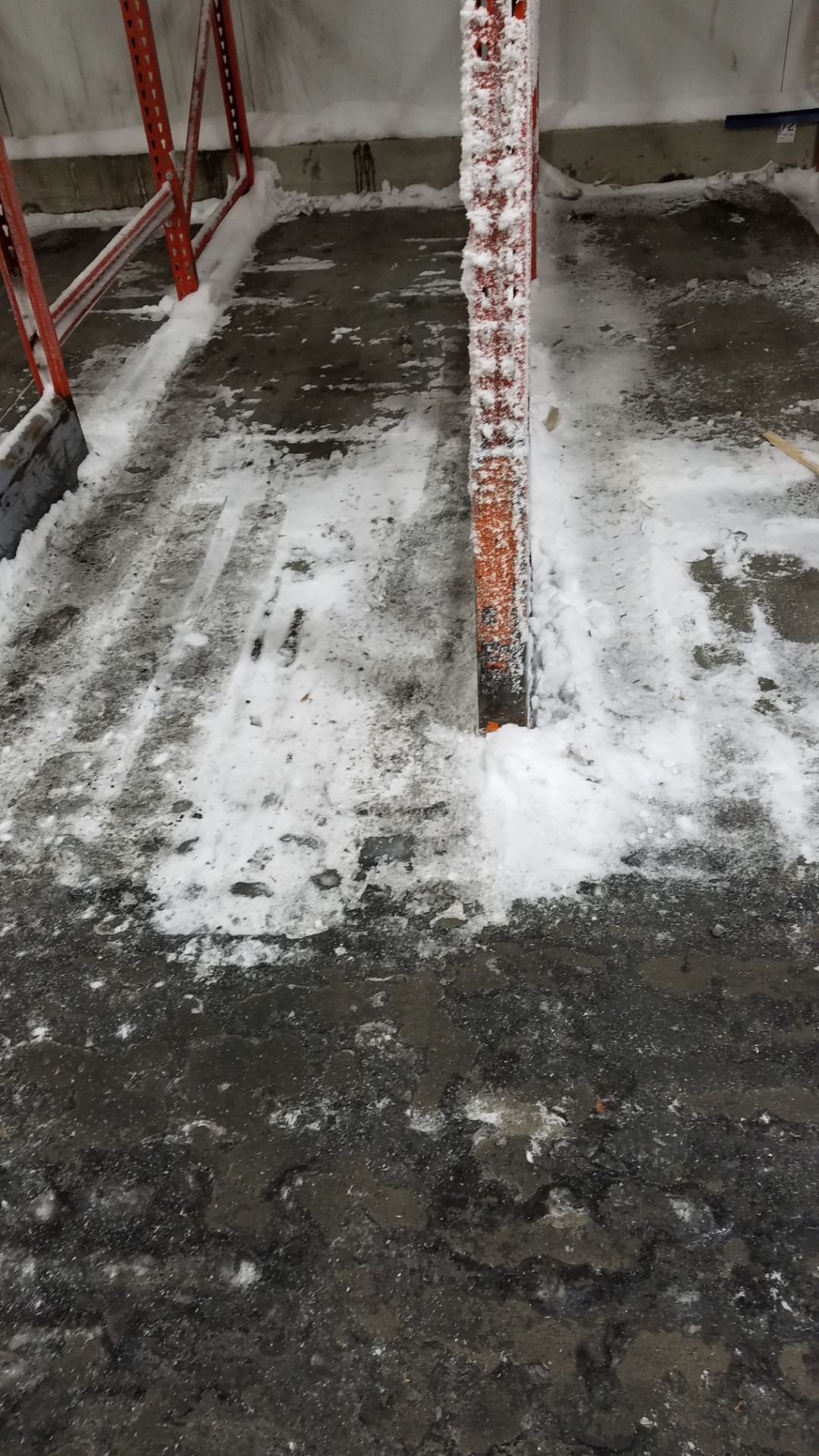 Warehouse floor covered in ice and snow around a red rack, likely due to a leak.