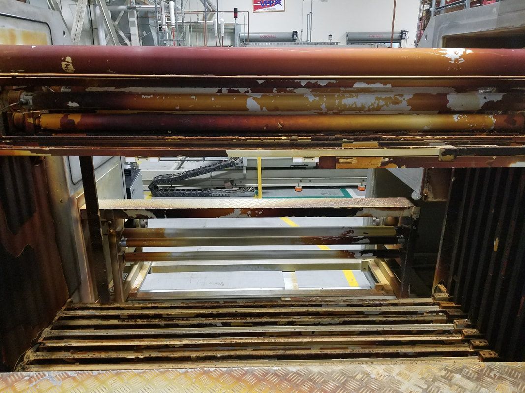 Rusty metal industrial equipment with visible pipes and rails, looking into a workspace.