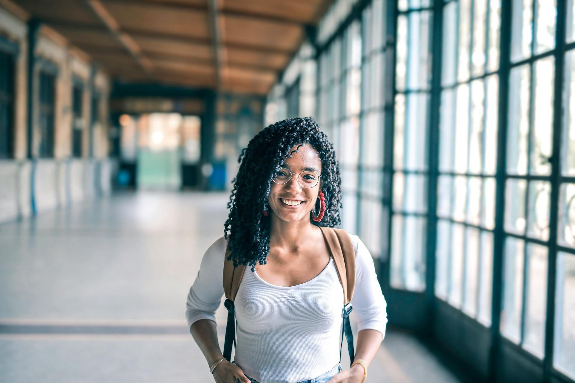 Smiling woman in a bright corridor with large windows and a backpack
