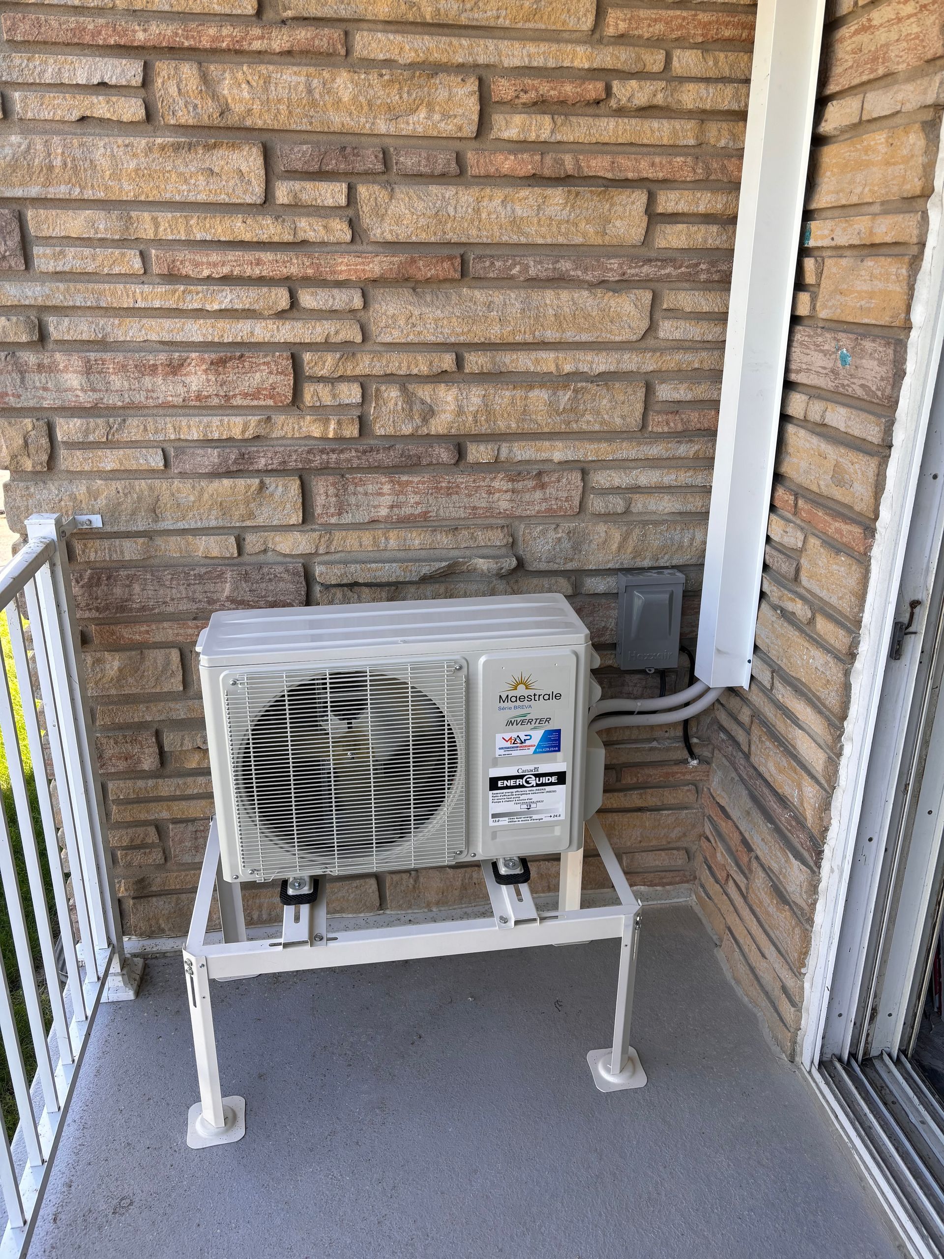 Un climatiseur est installé sur un balcon à côté d'un mur de briques.