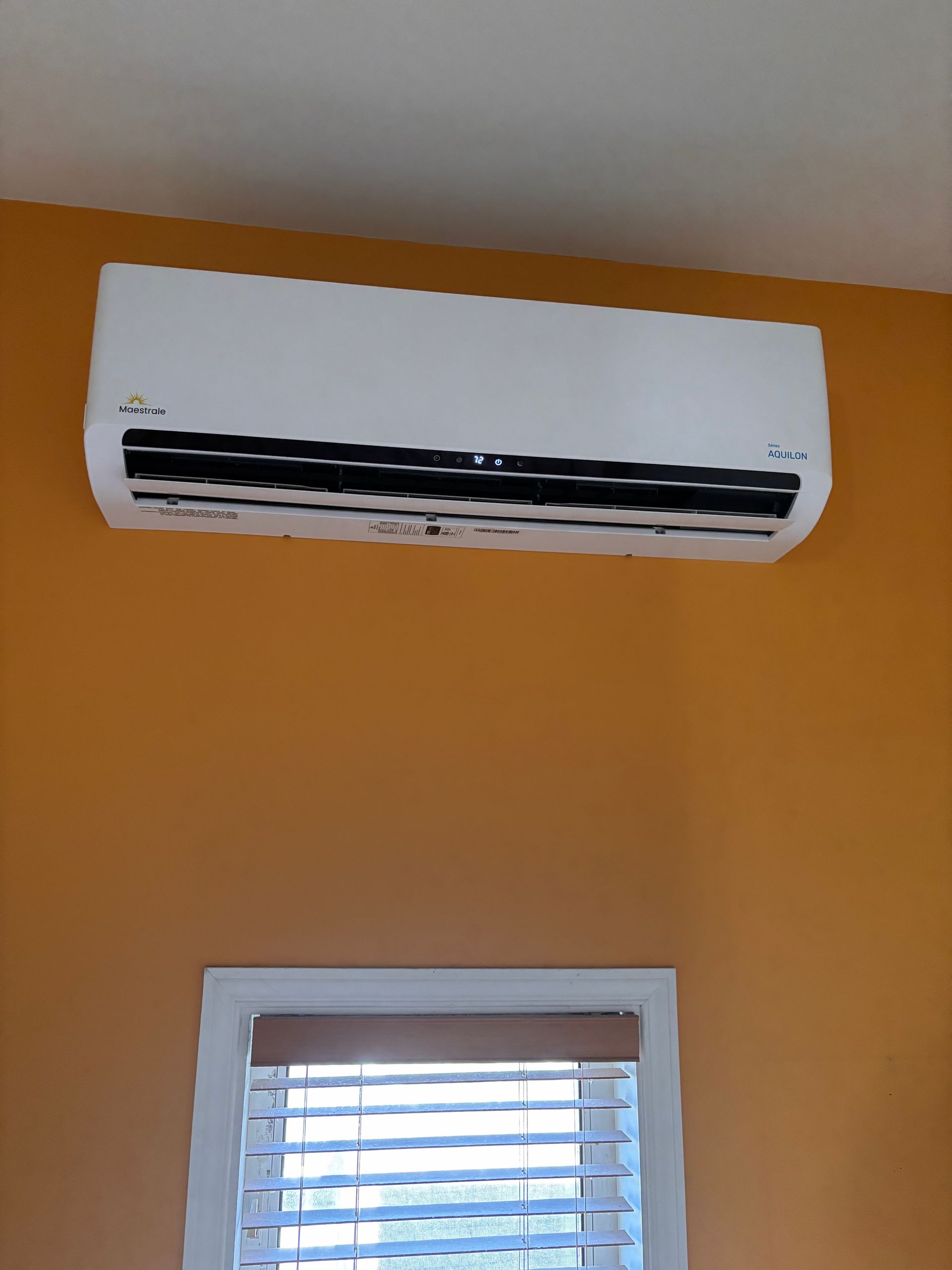 Un climatiseur blanc est accroché sur un mur jaune à côté d'une fenêtre.