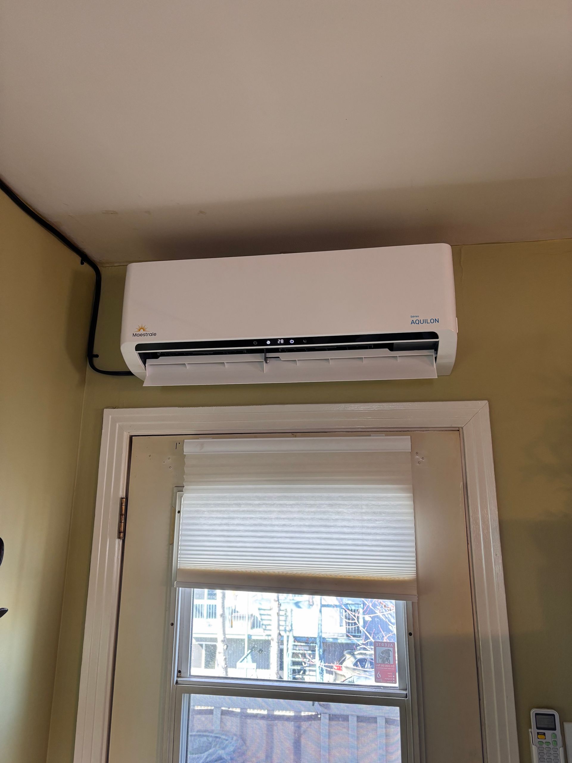 Un climatiseur blanc est suspendu au plafond au-dessus d'une fenêtre.