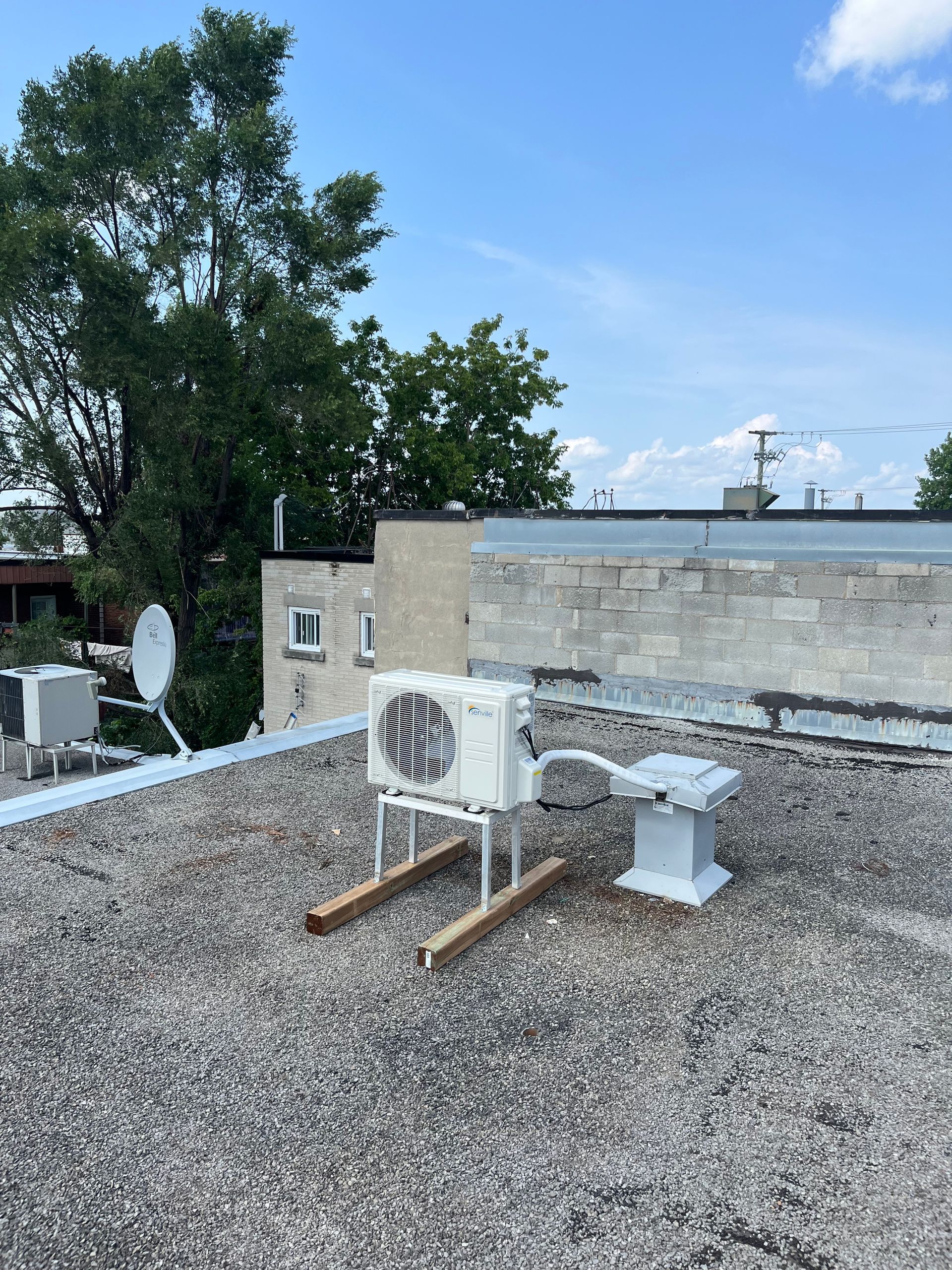 Un climatiseur blanc est posé sur un toit en gravier.