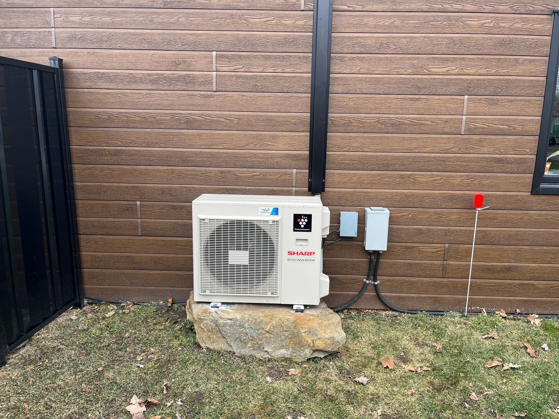 Un climatiseur blanc est posé sur un rocher devant un mur de briques.