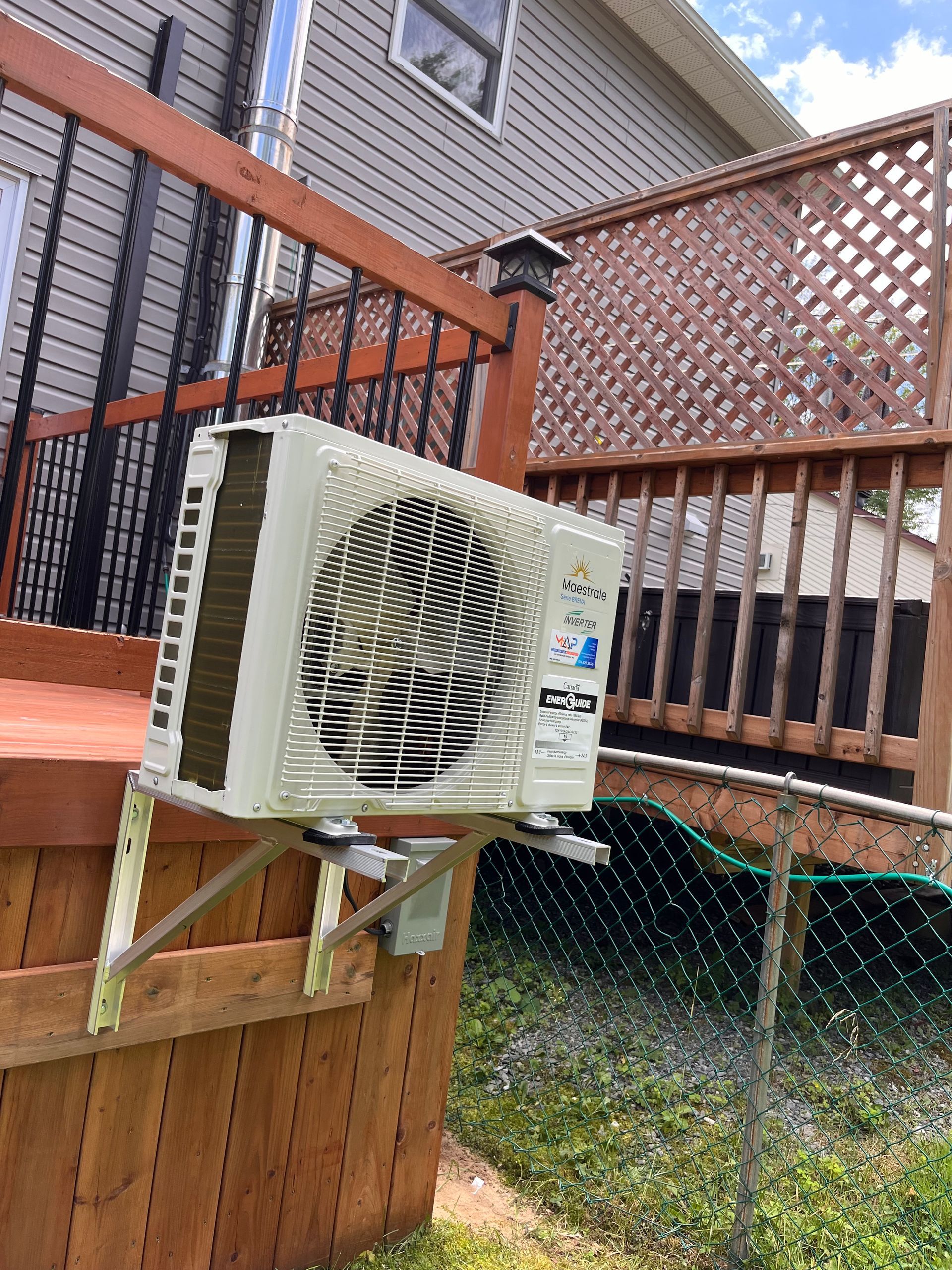 Un climatiseur est monté sur une terrasse en bois à côté d'une maison.