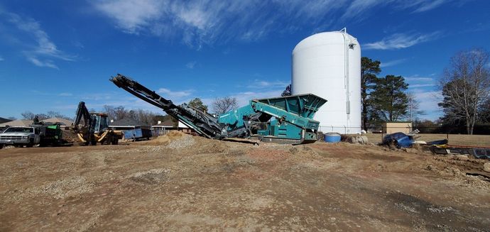 Construction site with large machinery, white tank, blue sky. Gravel crushing operation