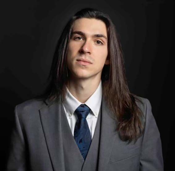 A young man with long hair is wearing a suit and tie.