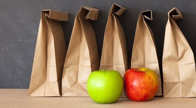A green apple sits in front of a row of brown paper bags