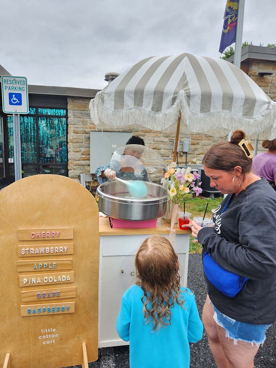 A woman and child are standing in front of a cotton candy stand