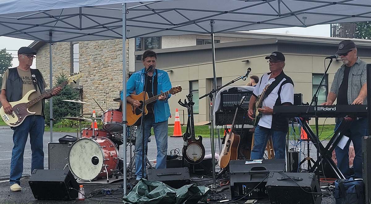 A group of men are playing guitars and a keyboard under a tent