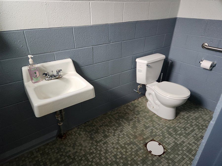 A bathroom with a toilet a sink and a soap dispenser