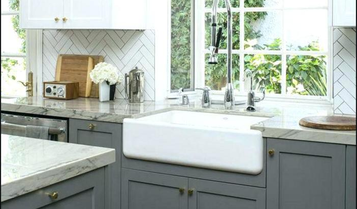 A kitchen with gray cabinets and a white farmhouse sink.